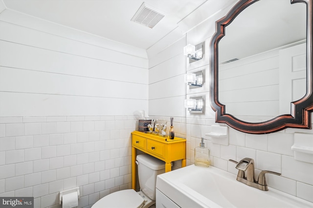 half bathroom with visible vents, a sink, tile walls, toilet, and backsplash