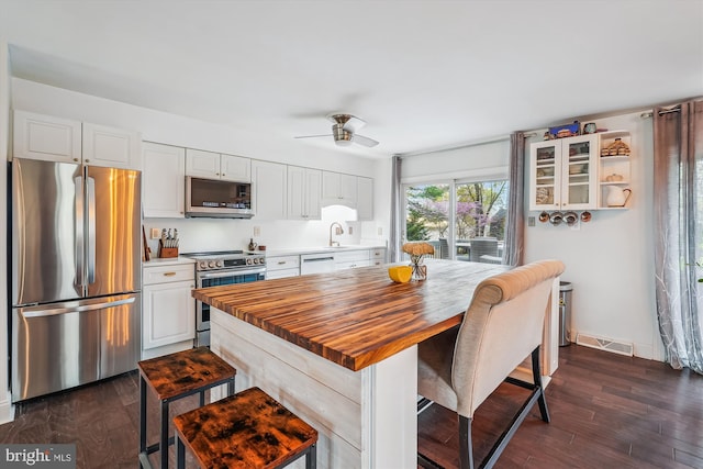 kitchen featuring white cabinets, a breakfast bar, visible vents, stainless steel appliances, and wooden counters