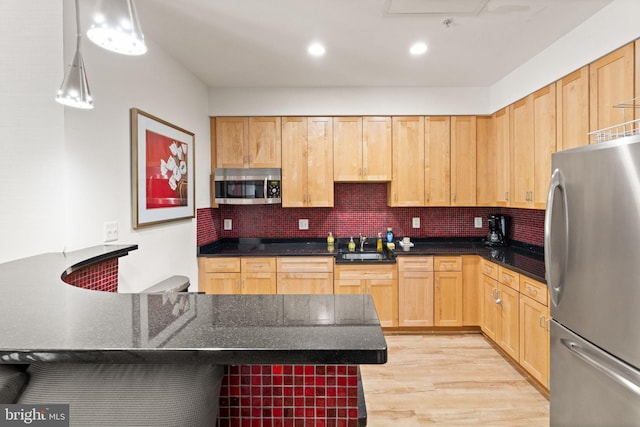 kitchen featuring stainless steel appliances, light brown cabinets, a sink, and tasteful backsplash