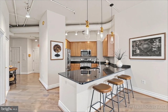 kitchen with track lighting, stainless steel appliances, light wood-style flooring, a kitchen bar, and a peninsula