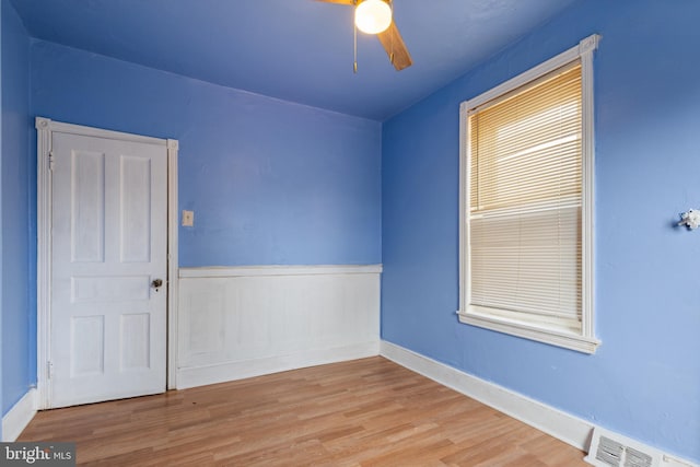 empty room featuring wood finished floors, visible vents, ceiling fan, and wainscoting