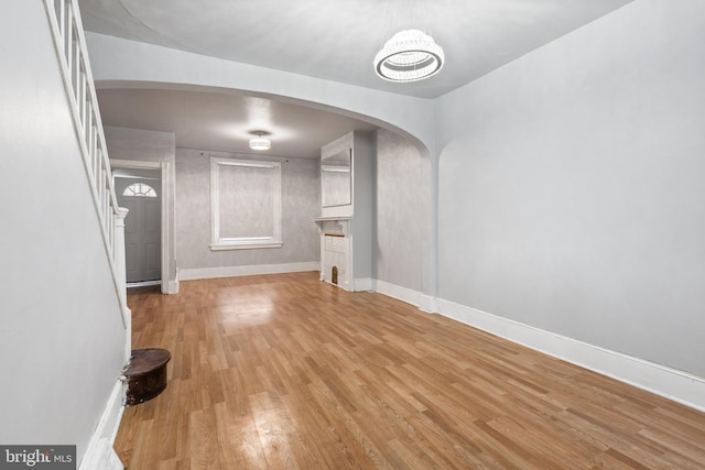 unfurnished living room with arched walkways, wood finished floors, and baseboards