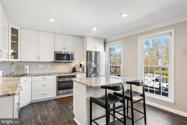 kitchen featuring light stone countertops, a sink, ornamental molding, and stainless steel appliances