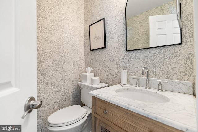 half bathroom with vanity, toilet, and wallpapered walls