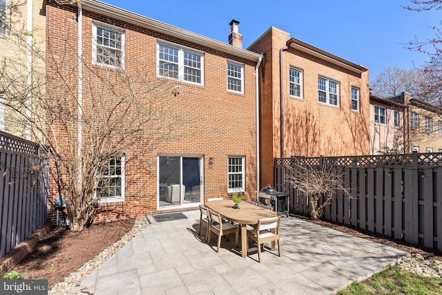 rear view of property with a fenced backyard, a patio, outdoor dining space, and brick siding
