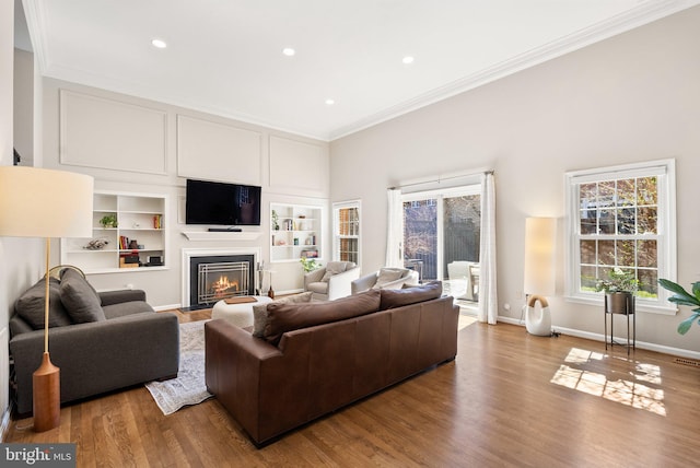 living area with a fireplace with flush hearth, ornamental molding, plenty of natural light, and recessed lighting