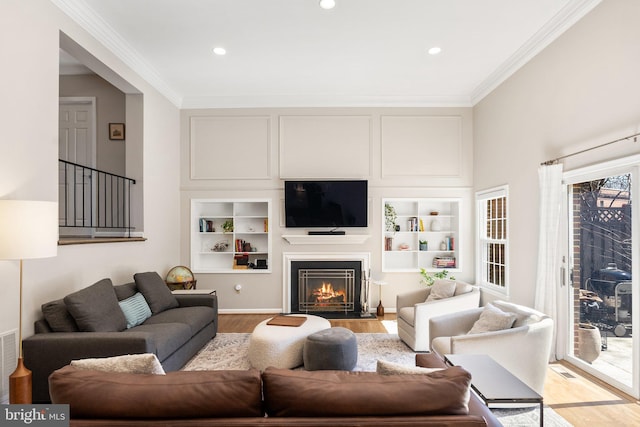 living area featuring built in features, recessed lighting, a fireplace with flush hearth, light wood-type flooring, and ornamental molding