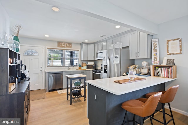 kitchen with a sink, a kitchen breakfast bar, stainless steel appliances, a peninsula, and light wood-type flooring