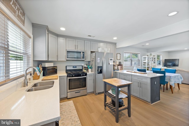 kitchen with a sink, appliances with stainless steel finishes, gray cabinets, and light wood-type flooring