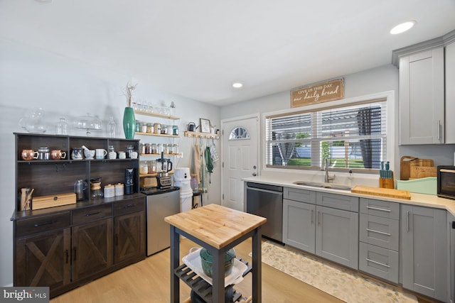kitchen featuring a sink, light wood finished floors, dishwasher, and gray cabinetry