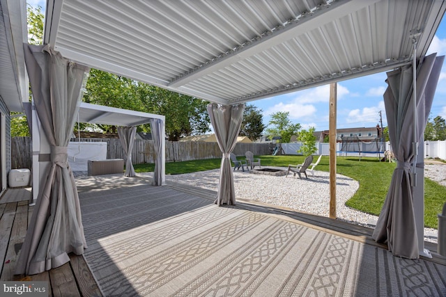 wooden deck with a yard, a fenced backyard, a trampoline, and an outdoor fire pit