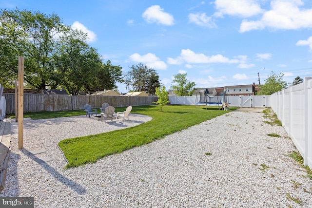 view of yard featuring a trampoline, a gate, a fenced backyard, an outdoor fire pit, and a patio