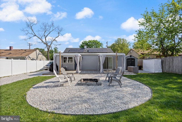 back of house with a shed, roof mounted solar panels, a lawn, an outdoor structure, and a fire pit