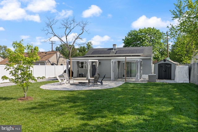 rear view of house featuring a patio, a fenced backyard, an outdoor fire pit, a storage shed, and solar panels