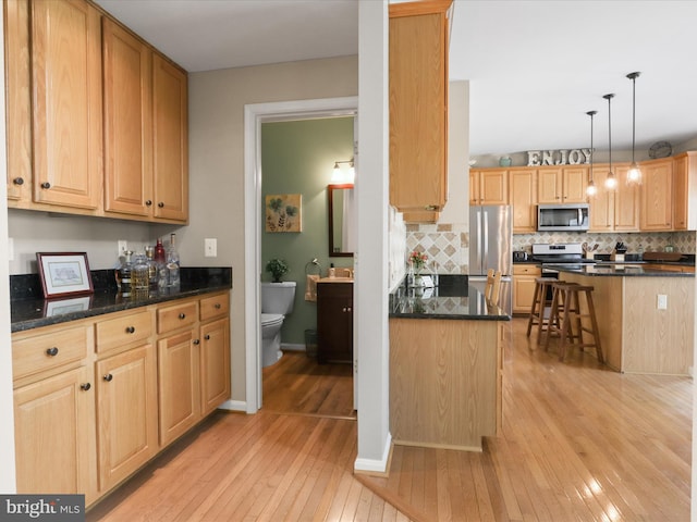 kitchen featuring dark stone counters, decorative backsplash, light wood finished floors, appliances with stainless steel finishes, and light brown cabinetry