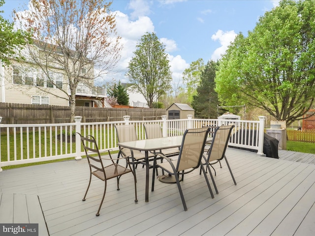 deck with a shed, a yard, a fenced backyard, outdoor dining space, and an outbuilding