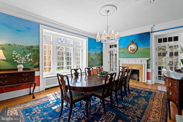 dining area with a chandelier, a fireplace, crown molding, wood finished floors, and french doors