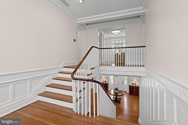stairway with crown molding, hardwood / wood-style floors, wainscoting, and visible vents
