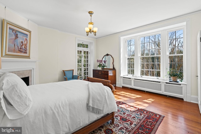 bedroom featuring an inviting chandelier, a tiled fireplace, crown molding, radiator heating unit, and hardwood / wood-style floors