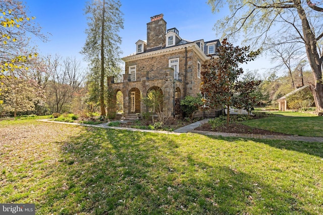 view of front of house featuring a chimney, stone siding, a front lawn, and a balcony