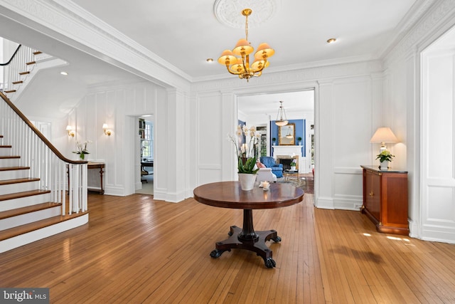 foyer entrance with an inviting chandelier, a decorative wall, crown molding, stairway, and hardwood / wood-style floors