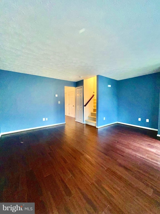 unfurnished room featuring stairs, baseboards, a textured ceiling, and wood finished floors