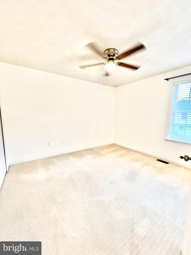 carpeted spare room with visible vents, baseboards, and ceiling fan