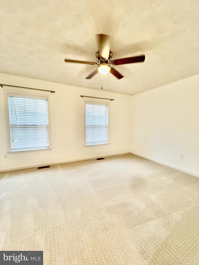 carpeted spare room with visible vents, ceiling fan, baseboards, and a textured ceiling