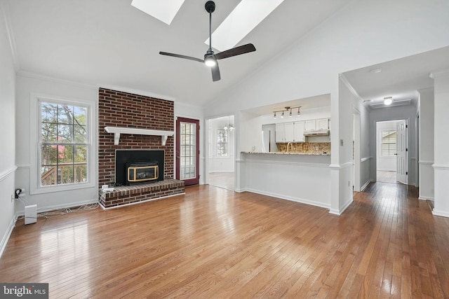 unfurnished living room with baseboards, light wood-type flooring, a ceiling fan, and a skylight