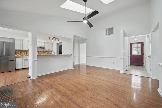 unfurnished living room with light wood-style flooring, a skylight, high vaulted ceiling, and visible vents