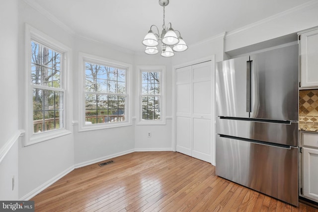 unfurnished dining area with visible vents, light wood-style flooring, a notable chandelier, and a healthy amount of sunlight