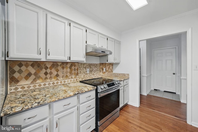 kitchen with light wood-style floors, stainless steel range with electric cooktop, light stone countertops, ornamental molding, and under cabinet range hood