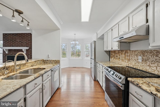 kitchen featuring a sink, appliances with stainless steel finishes, under cabinet range hood, light wood finished floors, and decorative backsplash