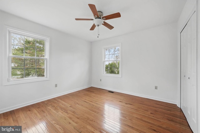 unfurnished bedroom featuring a closet, a ceiling fan, visible vents, wood-type flooring, and baseboards