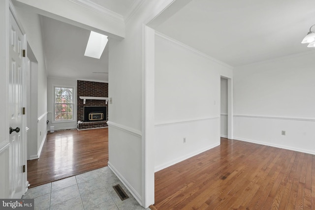 foyer entrance with ornamental molding, visible vents, a skylight, wood finished floors, and a brick fireplace