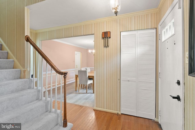 entryway featuring wallpapered walls, hardwood / wood-style flooring, stairway, crown molding, and a chandelier