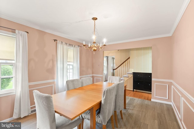 dining room with a chandelier, light wood-type flooring, wainscoting, ornamental molding, and stairs