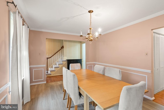 dining area with a chandelier, stairway, crown molding, wood finished floors, and a wainscoted wall