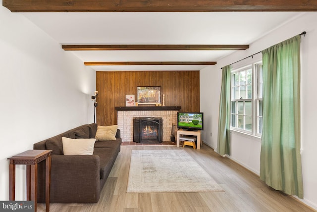 living area with a brick fireplace, light wood-style flooring, beam ceiling, and baseboards