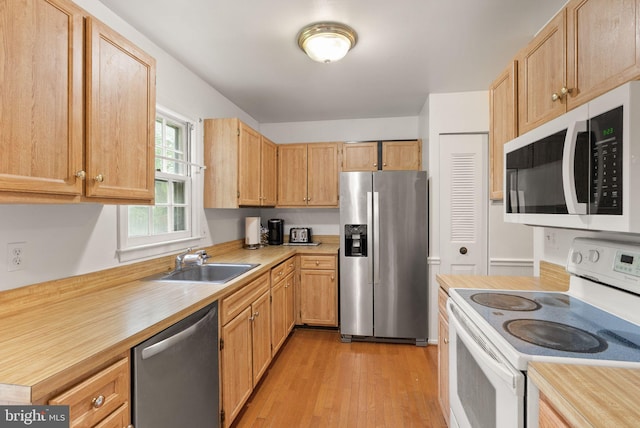 kitchen with stainless steel appliances, a sink, light countertops, light wood finished floors, and light brown cabinets