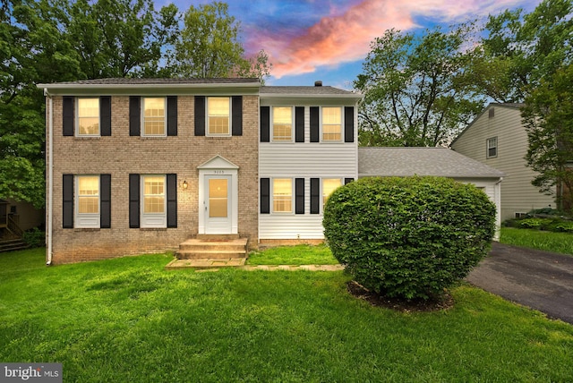 colonial-style house featuring a yard, driveway, brick siding, and a shingled roof