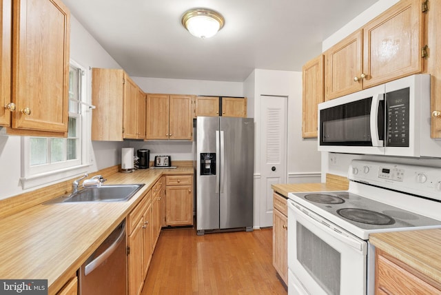 kitchen featuring stainless steel appliances, light countertops, a sink, light wood-style flooring, and light brown cabinets