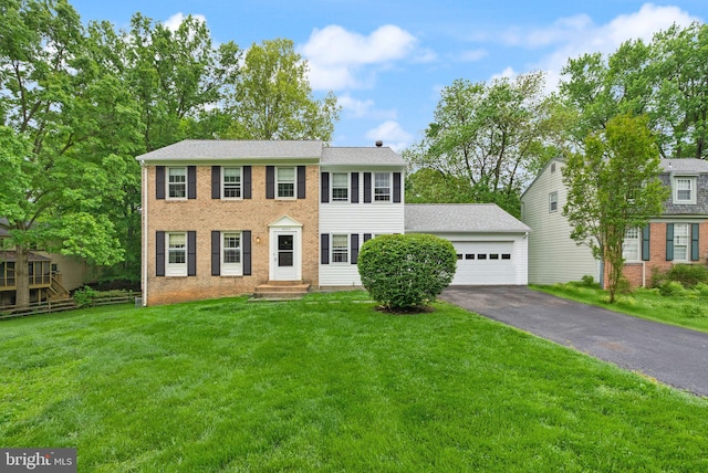 colonial house with asphalt driveway, a front lawn, an attached garage, and brick siding