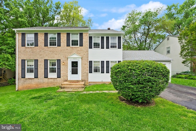 colonial-style house featuring a front lawn, driveway, brick siding, roof with shingles, and an attached garage