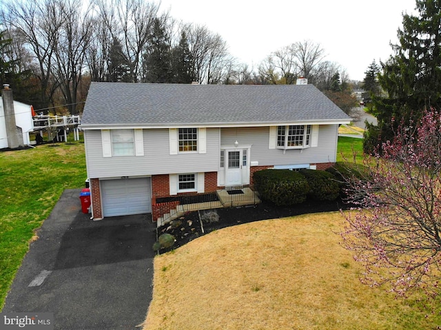 raised ranch featuring a front yard, roof with shingles, driveway, and an attached garage