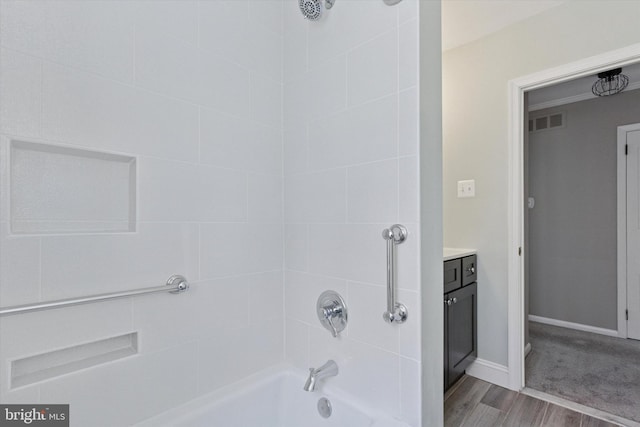 bathroom featuring vanity, visible vents, wood finished floors, washtub / shower combination, and baseboards