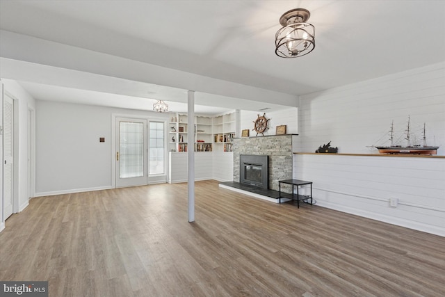 unfurnished living room with a chandelier, wood finished floors, a fireplace, and baseboards
