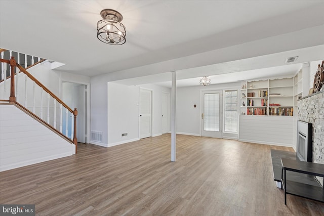 unfurnished living room with visible vents, a fireplace, wood finished floors, and stairs