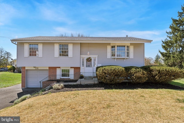 split foyer home featuring a garage, roof with shingles, a front yard, brick siding, and driveway