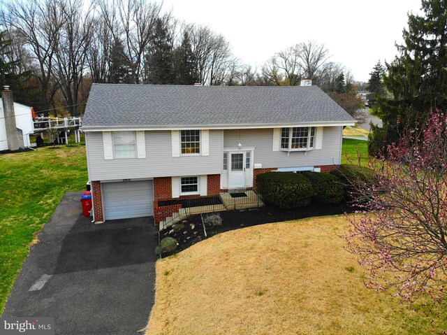 raised ranch featuring roof with shingles, driveway, a front yard, and a garage
